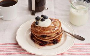 a stack of pancakes with blueberries and whipped cream on a white plate .