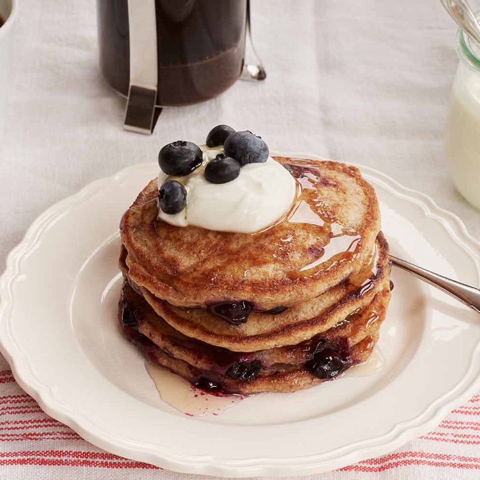 a stack of pancakes with blueberries and whipped cream on a white plate .