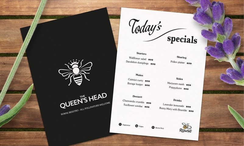 a menu for the queen 's head restaurant is sitting on a wooden table next to purple flowers .