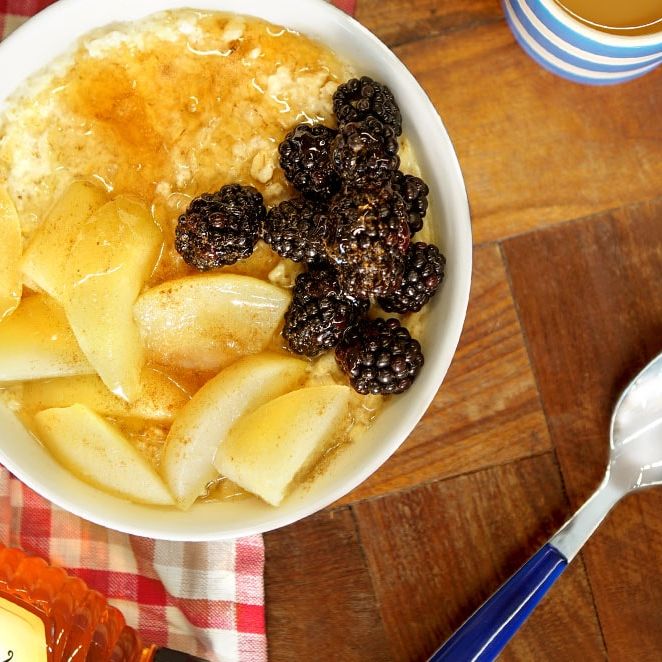 a bowl of oatmeal with apples , blackberries and honey next to a bottle of honey .
