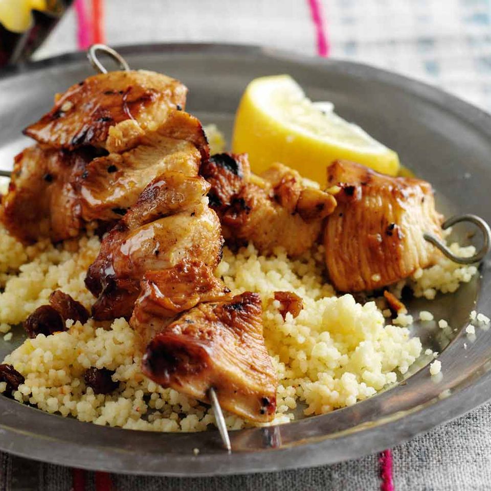 a plate of food with chicken skewers and couscous on a table .