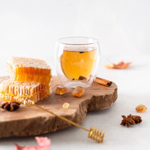a glass of tea is sitting on a wooden cutting board next to honeycomb and cinnamon sticks .