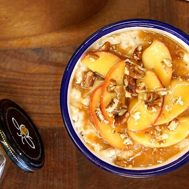 a bowl of oatmeal with apples and pecans on a wooden table next to a jar of Rowse honey .