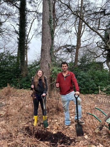 a man and a woman are standing next to each other in the woods holding shovels .