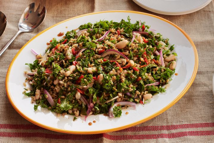a white plate topped with a salad of kale , beans , and onions on a table .