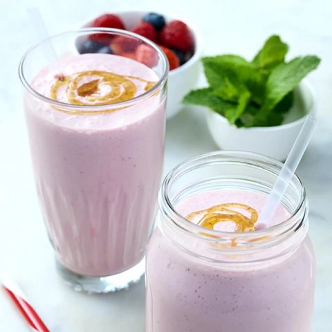 Two pink smoothies with honey swirls, next to bowls of berries and mint.