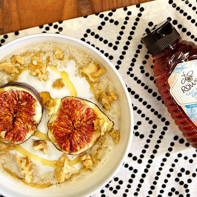 a bowl of oatmeal with figs , walnuts and honey next to a bottle of honey .