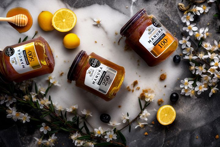 three jars of manuka honey are sitting on a table surrounded by lemons and flowers .