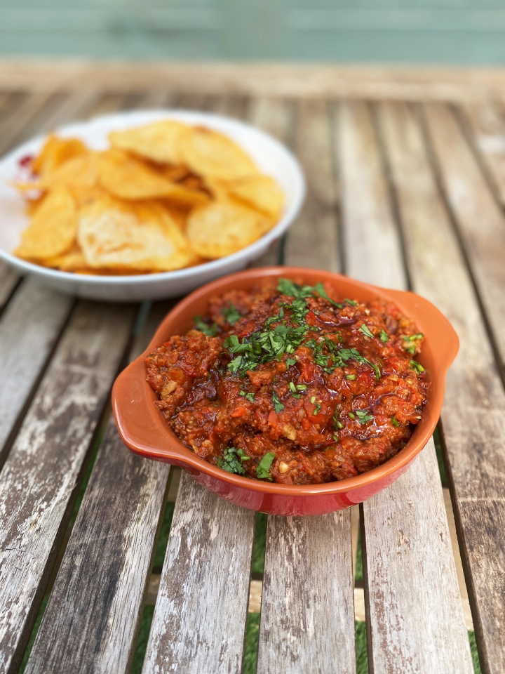 a bowl of smokey red pepper dip on a wooden table next to a bowl of chips