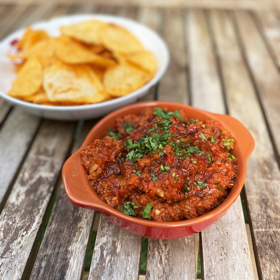 a bowl of smokey red pepper dip on a wooden table next to a bowl of chips