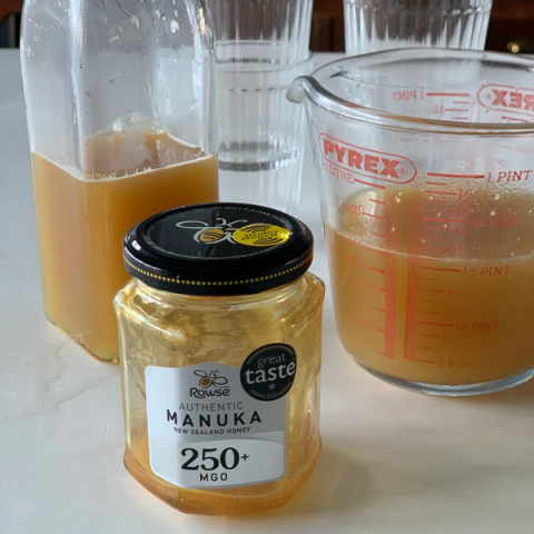 a jar of manuka honey next to a pyrex measuring cup