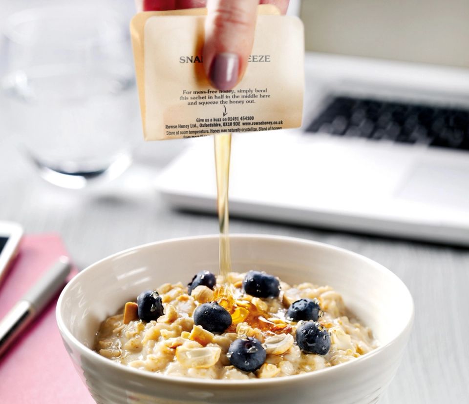 a person is pouring honey from Rowse Snap & Squeeze over a bowl of oatmeal with blueberries .