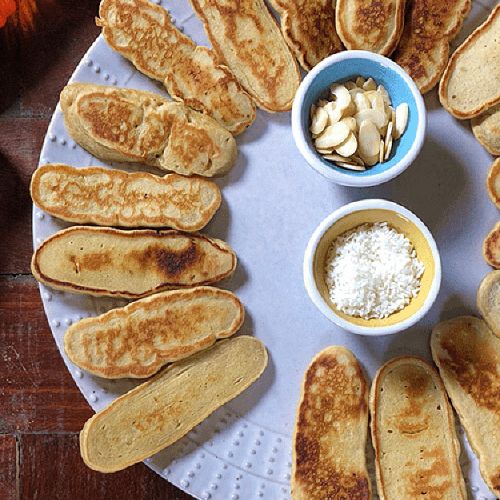 a white plate topped with pancakes and bowls of toppings on a wooden table .