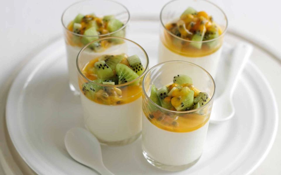 four cups of dessert with kiwi and passion fruit on a white plate .