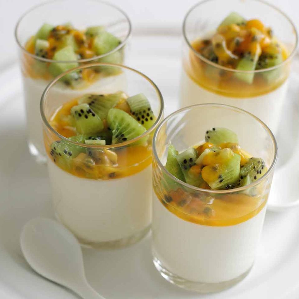 four cups of dessert with kiwi and passion fruit on a white plate .