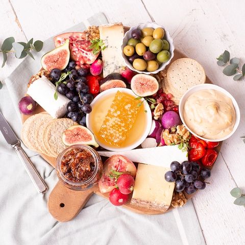 a wooden cutting board topped with cheese , fruit , olives , crackers and honey .