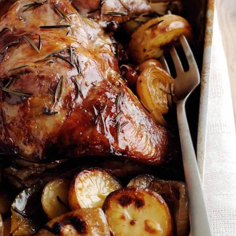 Roasted lamb with glistening rosemary, potatoes, and onions in a pan, with a fork.