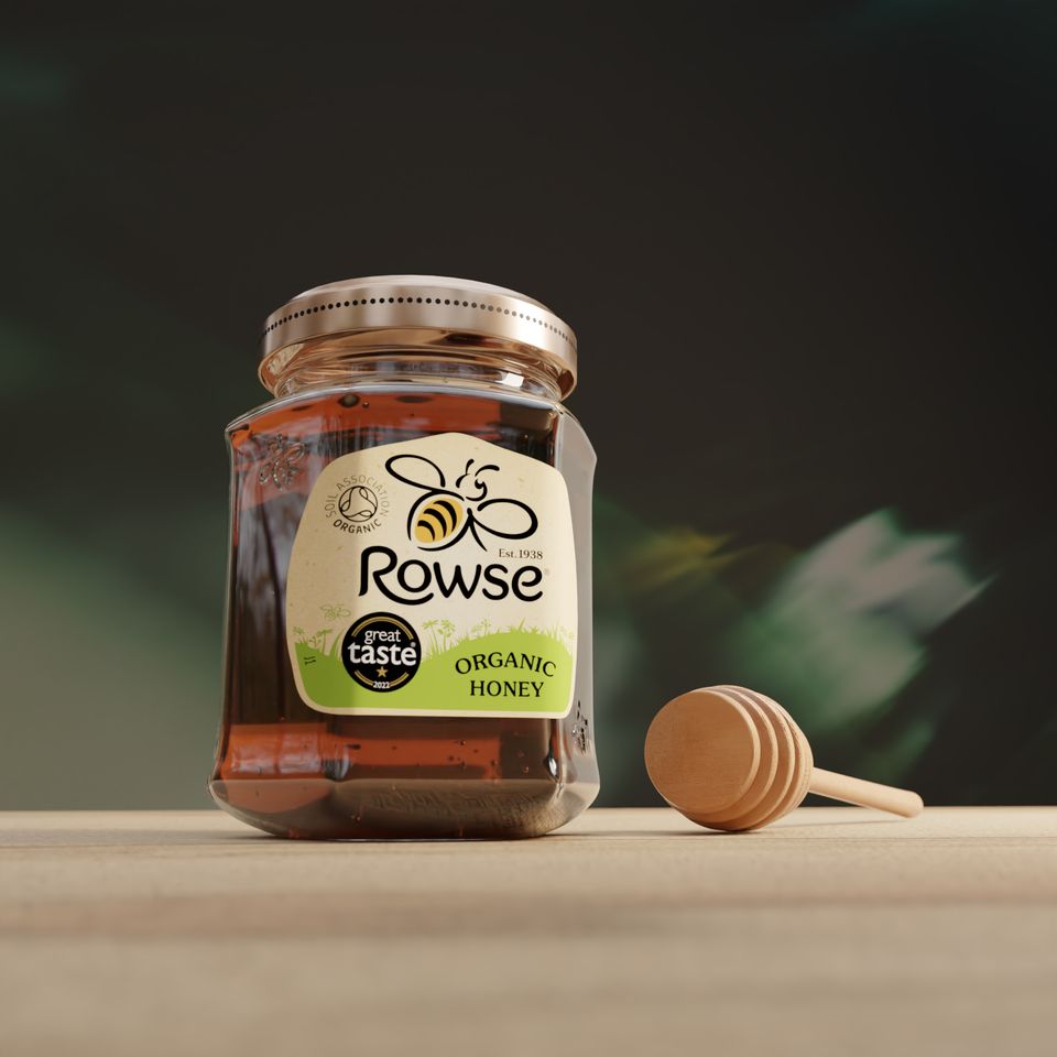 A jar of Rowse organic honey and a wooden dipper on a table.