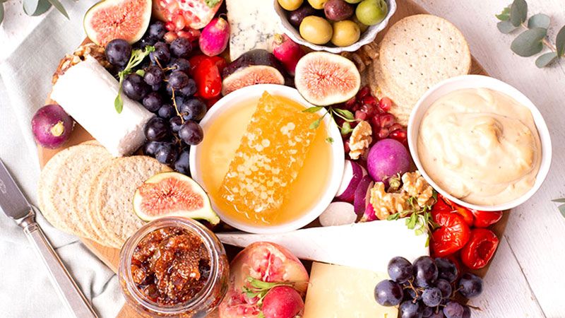 a wooden cutting board topped with cheese , fruit , crackers , olives and honeycomb .