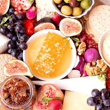 a wooden cutting board topped with cheese , fruit , crackers , olives and honeycomb .