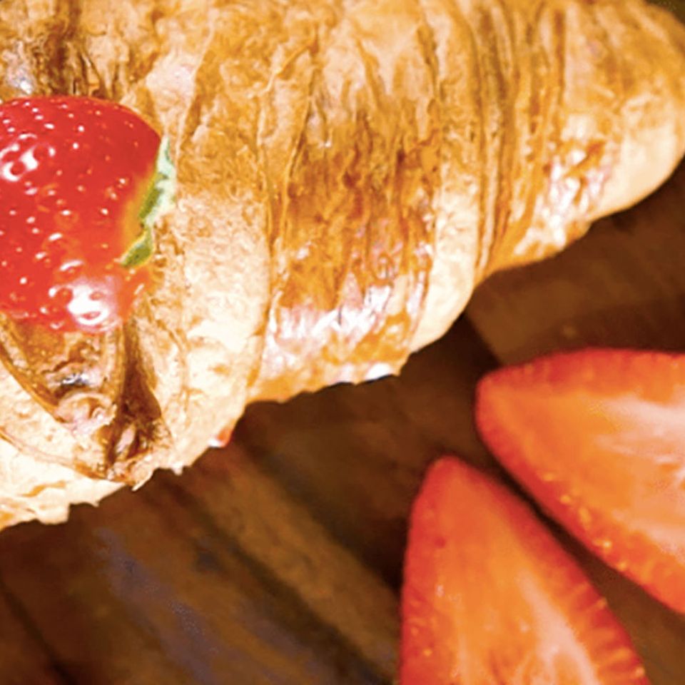 a croissant with a strawberry on top of it on a wooden table .