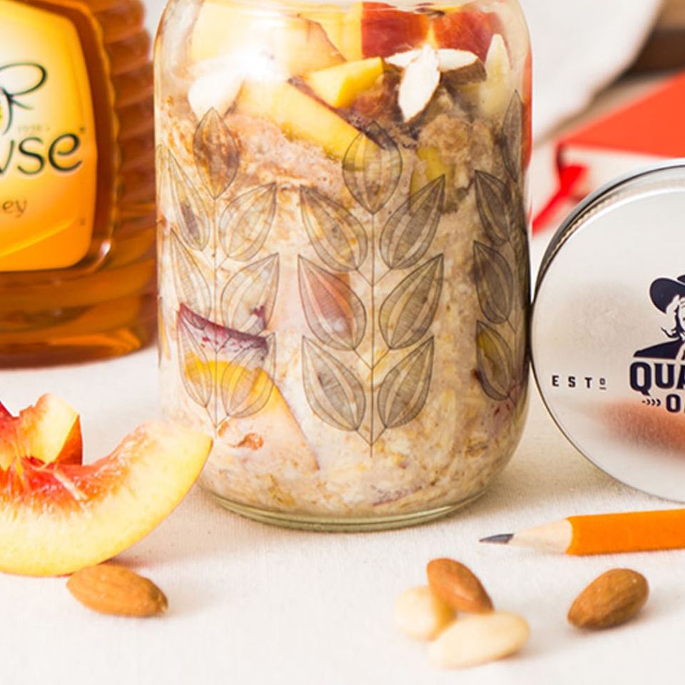 a jar of oatmeal with apples , almonds and honey next to a bottle of honey .