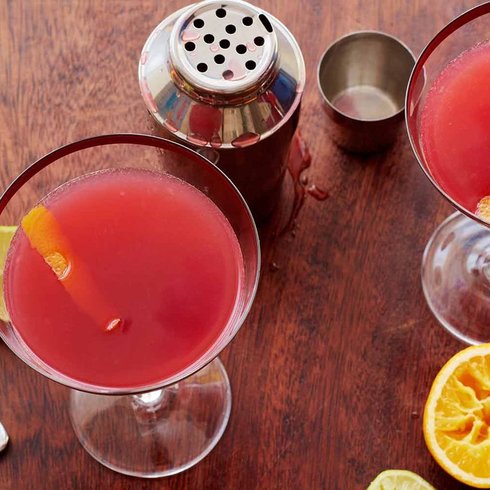 two martini glasses filled with red liquid and a fork on a wooden table .