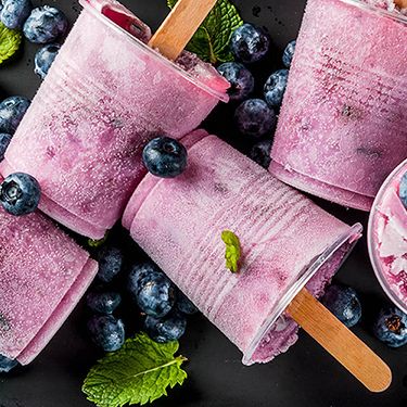 a close up of a plate of blueberry popsicles with blueberries and mint leaves .