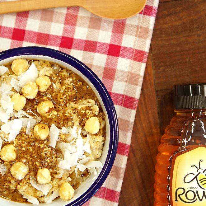 a bowl of oatmeal with nuts and coconut next to a bottle of honey .