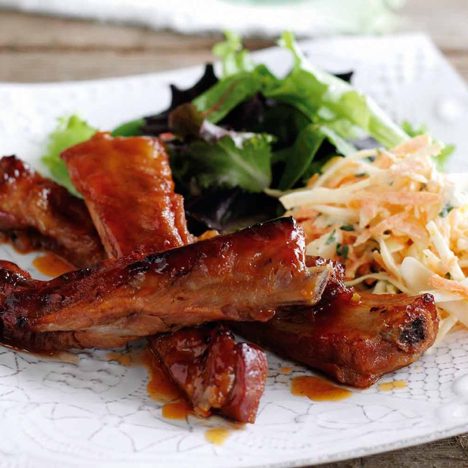 a white plate topped with ribs and coleslaw on a wooden table .