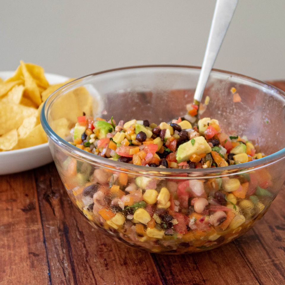 a bowl of salsa with a spoon in it is on a wooden table next to a bowl of chips .