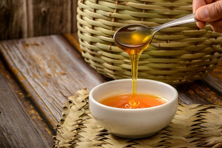 pouring honey from a spoon into a bowl .