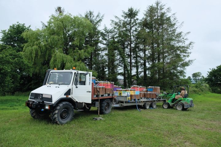 a white truck with a trailer full of bees is parked in a grassy field .