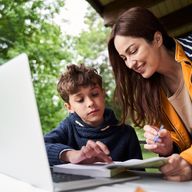 a woman is helping a young boy with his homework while looking at a laptop .