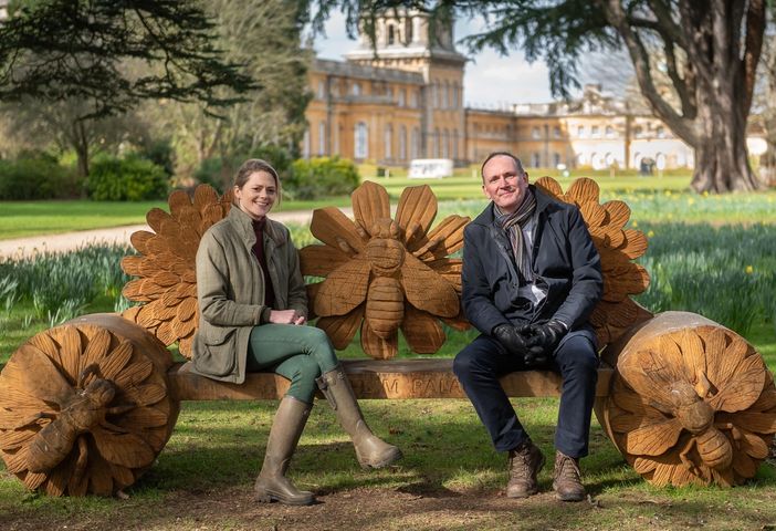 a man and a woman are sitting on a wooden bench in a park .