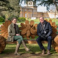 a man and a woman are sitting on a wooden bench in a park .