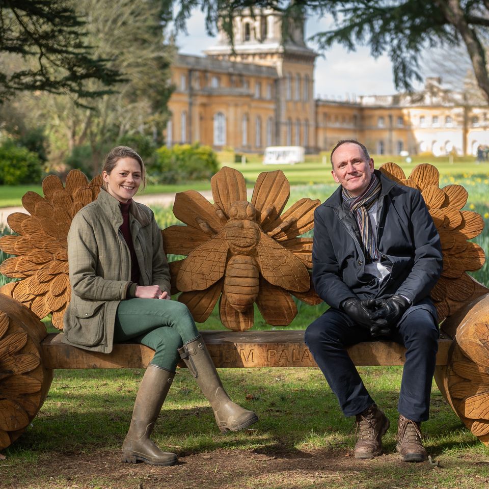 a man and a woman are sitting on a wooden bench in a park .