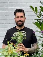 a man with a beard is holding a bouquet of flowers in front of a white brick wall .