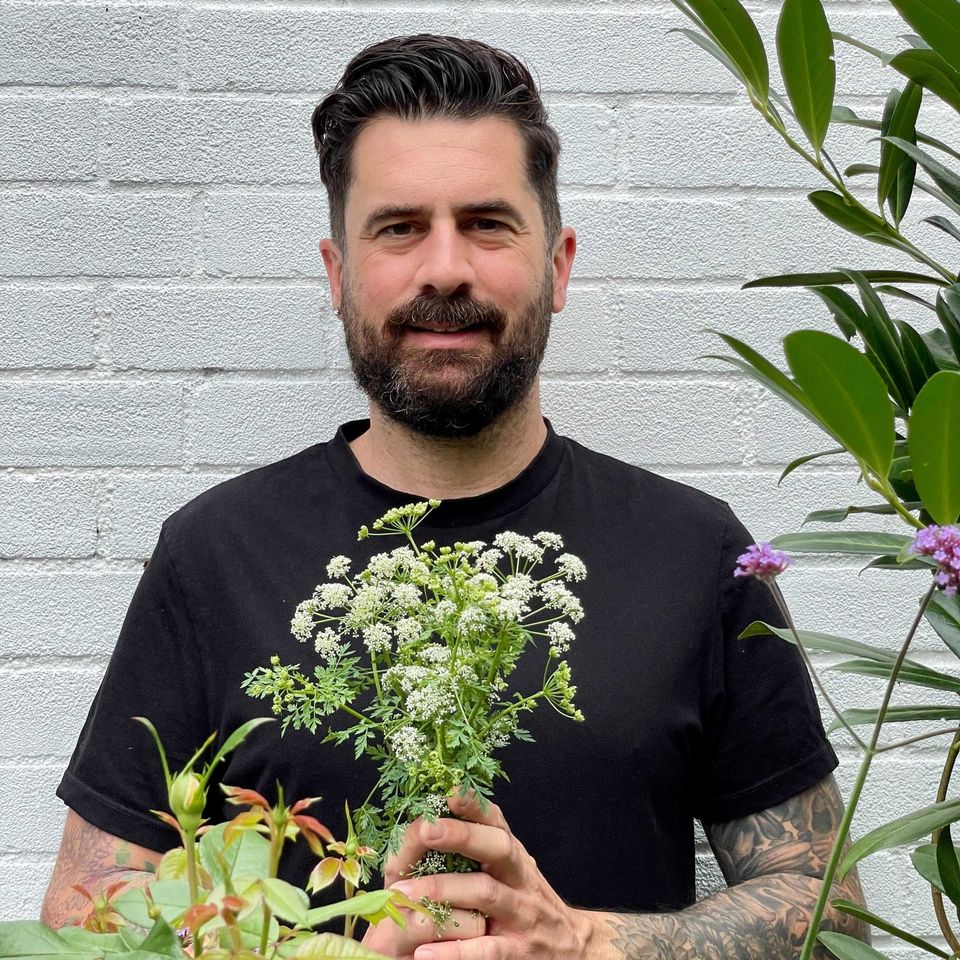 a man with a beard is holding a bouquet of flowers in front of a white brick wall .