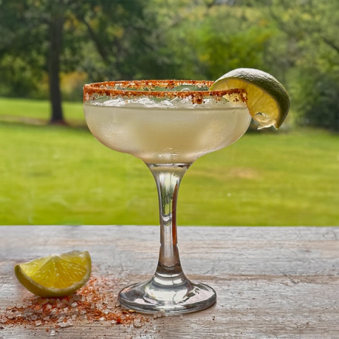 A margarita in a glass with a chili-lime rim and lime wedge, on a wooden table with a green background.