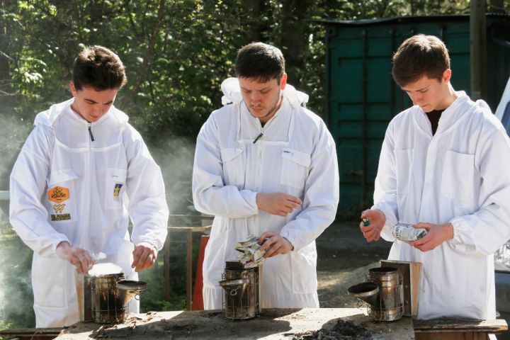 three young men in bee suits are standing around a table .