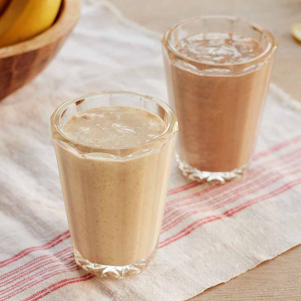 two smoothies are sitting on a table next to a bowl of bananas .