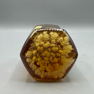 A hexagonal jar of dark amber honey with yellow mold growing inside.