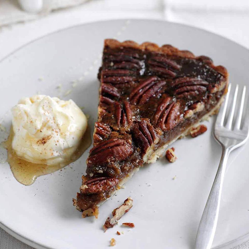 a slice of pecan pie with ice cream on a plate with a fork .