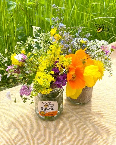 a jar of rowse honey sits next to a vase of flowers