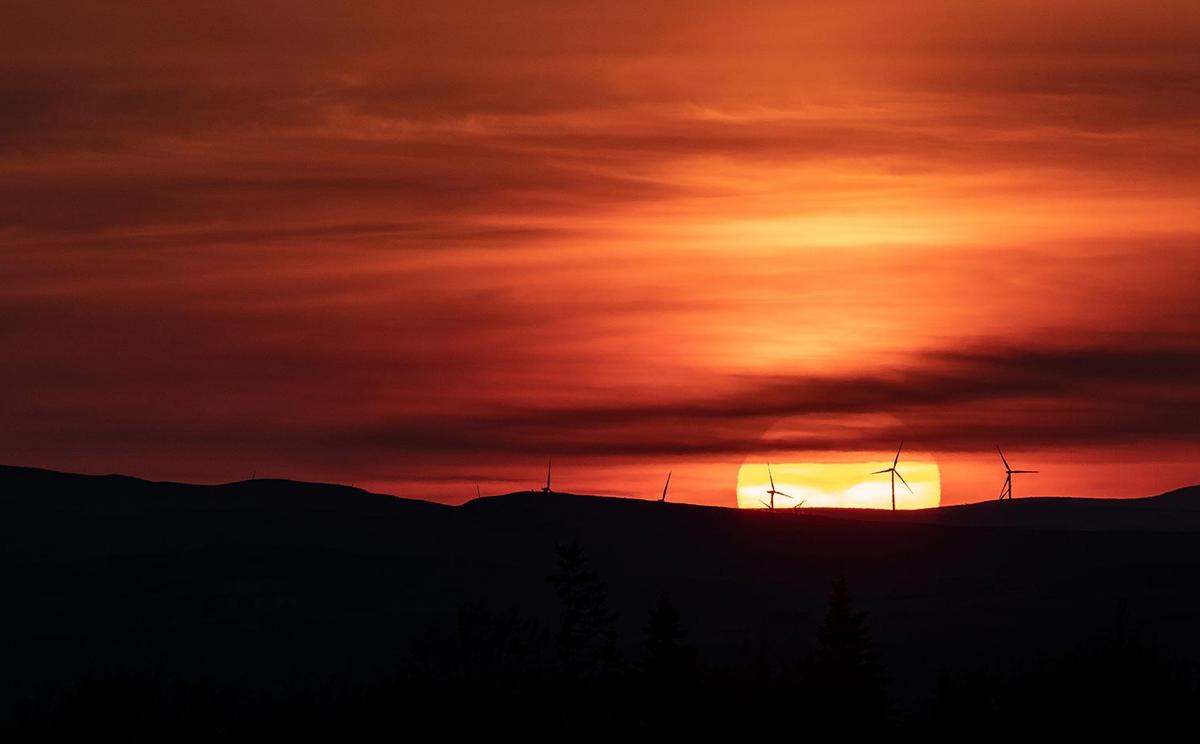 A crimson sky with the sun setting on the horizon behind some windmills