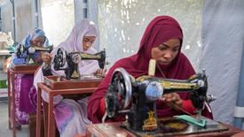 Three women in hijabs seated at sewing machines, concentrating on their work.