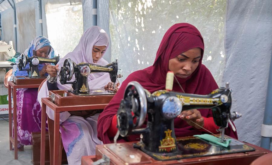 Three women in hijabs seated at sewing machines, concentrating on their work.