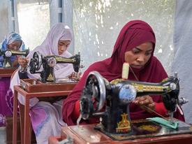 Three women in hijabs seated at sewing machines, concentrating on their work.