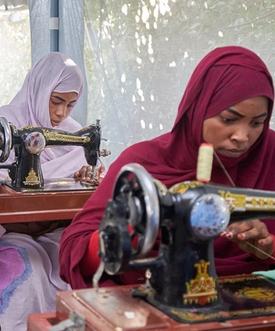 Three women in hijabs seated at sewing machines, concentrating on their work.
